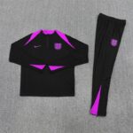 Black athletic tracksuit top and pants with purple accents, England crest on the chest and leg, laid flat on a gray carpet.