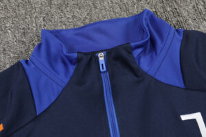 Close-up of a navy jacket with a bright blue zipper and collar on a gray carpet, with a small white logo partially visible.