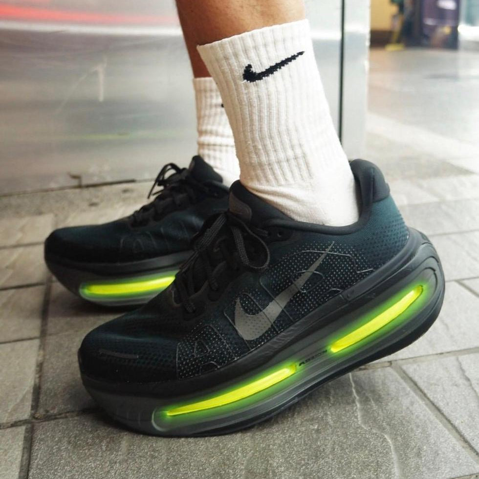 7c262a26-f6d1-4631-9352-c72e69c636b9 | UAE SPORT STORE Black Nike running shoes with bright green translucent air sole, white crew socks, standing on a paved sidewalk.