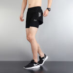 7c8620ef | UAE SPORT STORE Male model wearing black Under Armour athletic shorts with a built-in liner, paired with black Nike running shoes, standing in a neutral studio.