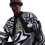 Person wearing a black-and-white swirling-pattern sports jersey with a Brazil crest and neon-green accents, sunglasses on.