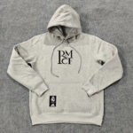 Gray hooded sweatshirt with a stacked RM CF logo on the chest and a Real Madrid tag on the front pocket, laid flat on a gray carpet.