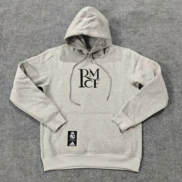 Gray hooded sweatshirt with a stacked RM CF logo on the chest and a Real Madrid tag on the front pocket, laid flat on a gray carpet.