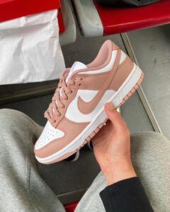 Pink and white Nike sneaker being held in one hand, showing a blush-pink overlay and white paneling.