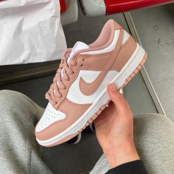 Pink and white Nike sneaker being held in one hand, showing a blush-pink overlay and white paneling.