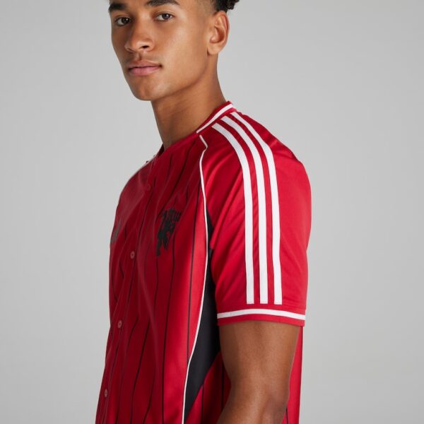 Young man wearing a red athletic jersey with white stripes on the sleeves, angled to camera, neutral background