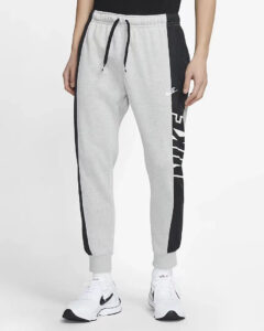 Grey Nike joggers with black side panels and drawstring waist, paired with white athletic sneakers on a standing model.