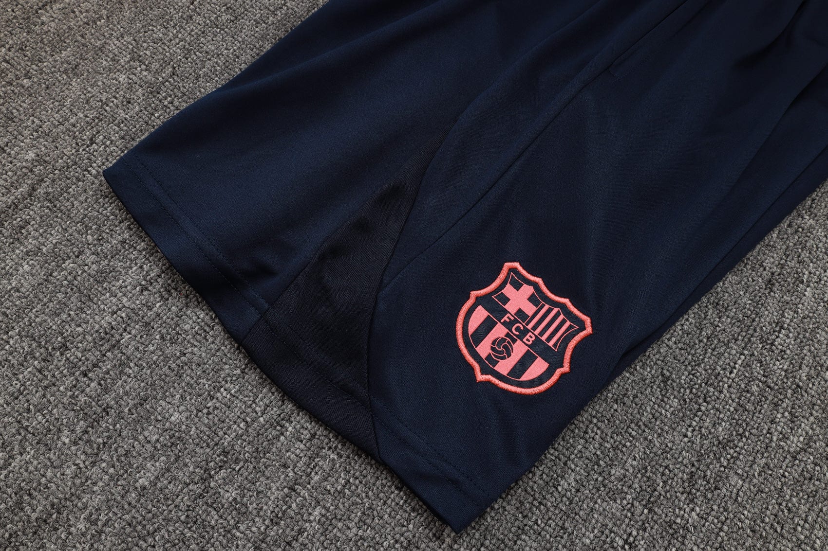 7d763b27 | UAE SPORT STORE Navy athletic pants with a pink FC Barcelona crest embroidered on the lower leg, laid on a grey carpet.