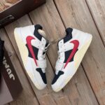 Pair of white, navy, and red Nike sneakers on a wooden deck beside a brown shoebox.