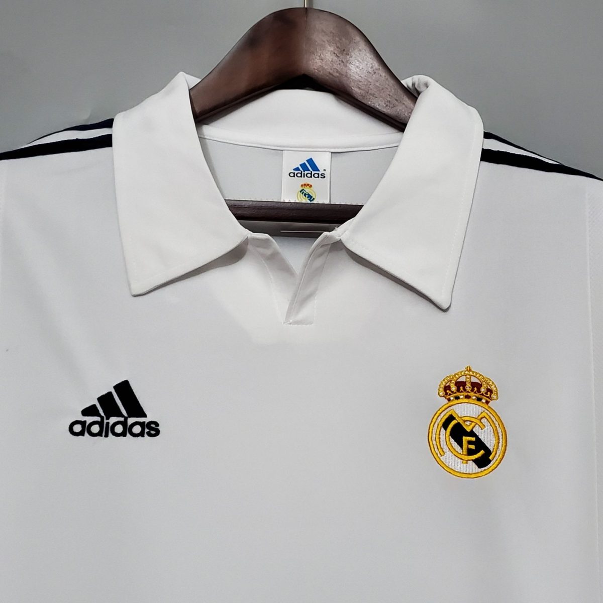 White Real Madrid football jersey on a hanger, showing the Adidas logo and club crest on the chest area.