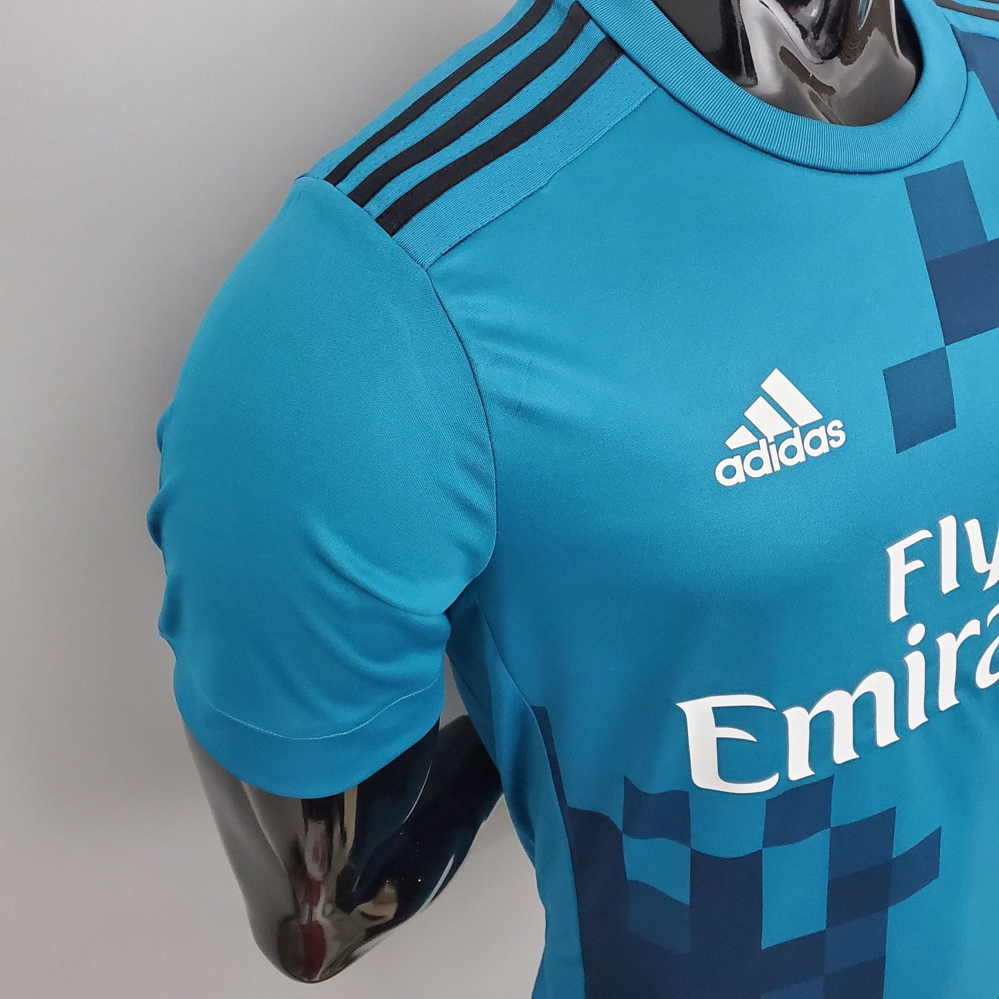 7e83efec_f55092a7-119d-4103-95b8-bbedfdb10900 | UAE SPORT STORE Close-up of a turquoise Adidas jersey shoulder showing the black three-stripe design and part of the Adidas logo on the chest.