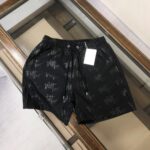 Black drawstring shorts with all-over Dior Paris print and white tag attached on a glass surface display.
