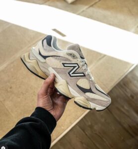 Beige and gray chunky sneaker held by a hand against a light stone staircase backdrop, outdoor setting.