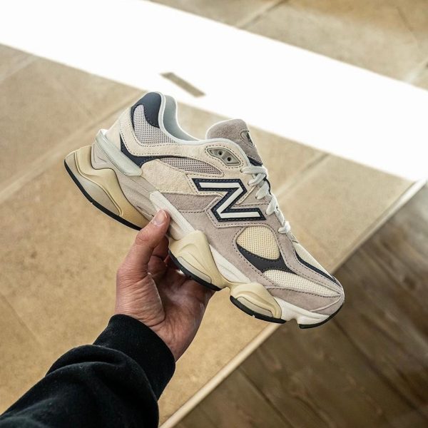 Beige and gray chunky sneaker held by a hand against a light stone staircase backdrop, outdoor setting.