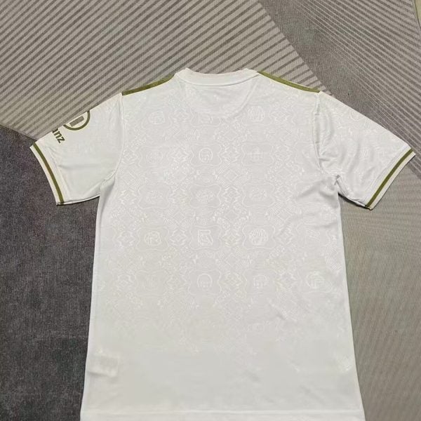 White soccer jersey laid flat, back view, with subtle tonal pattern and green trim on shoulders and sleeve edges
