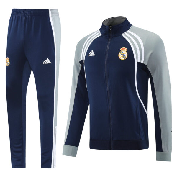 Navy Real Madrid tracksuit: zip-up jacket with light gray sleeves and white piping, Adidas logos, paired with matching navy pants with side stripes and team crest.