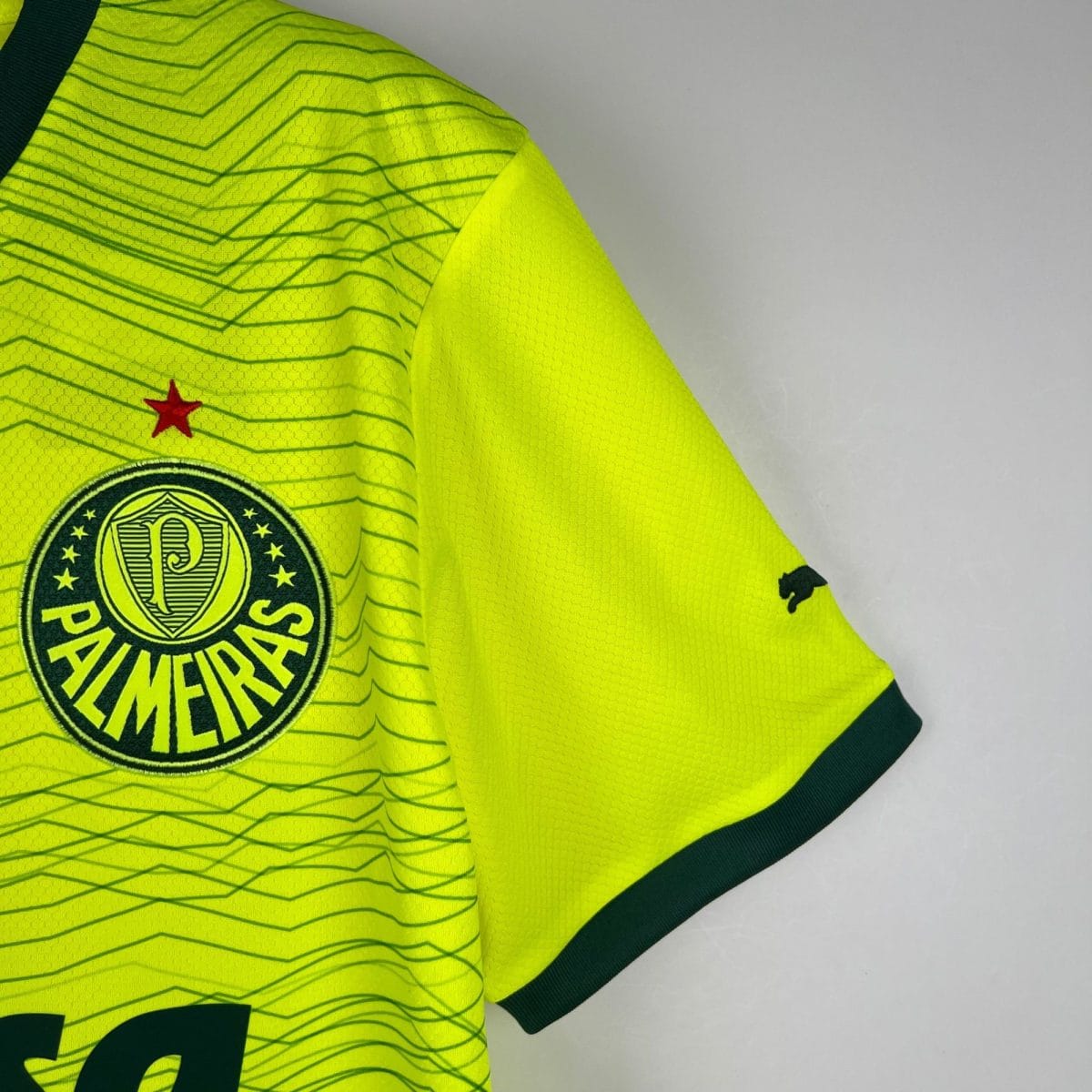 Close-up of a neon yellow sports jersey showing a circular crest with stars and green trim on the sleeve edge.