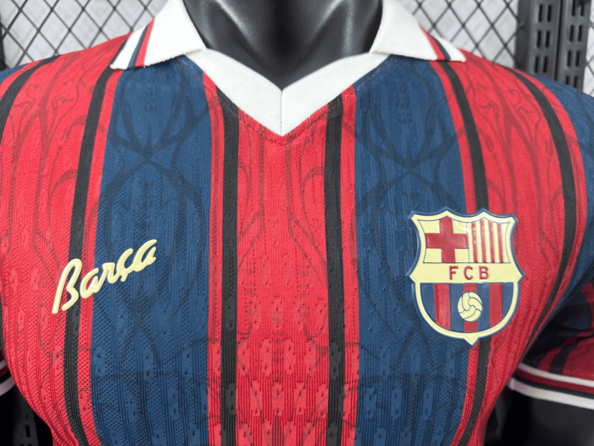 Close-up of a Barcelona FC jersey showing red and blue vertical stripes, white collar, and the Barça signature with the FCB crest on the chest.