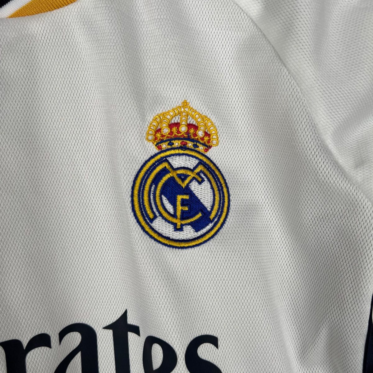 Close-up of white jersey fabric with a partial embroidered Real Madrid crest visible at the bottom edge.