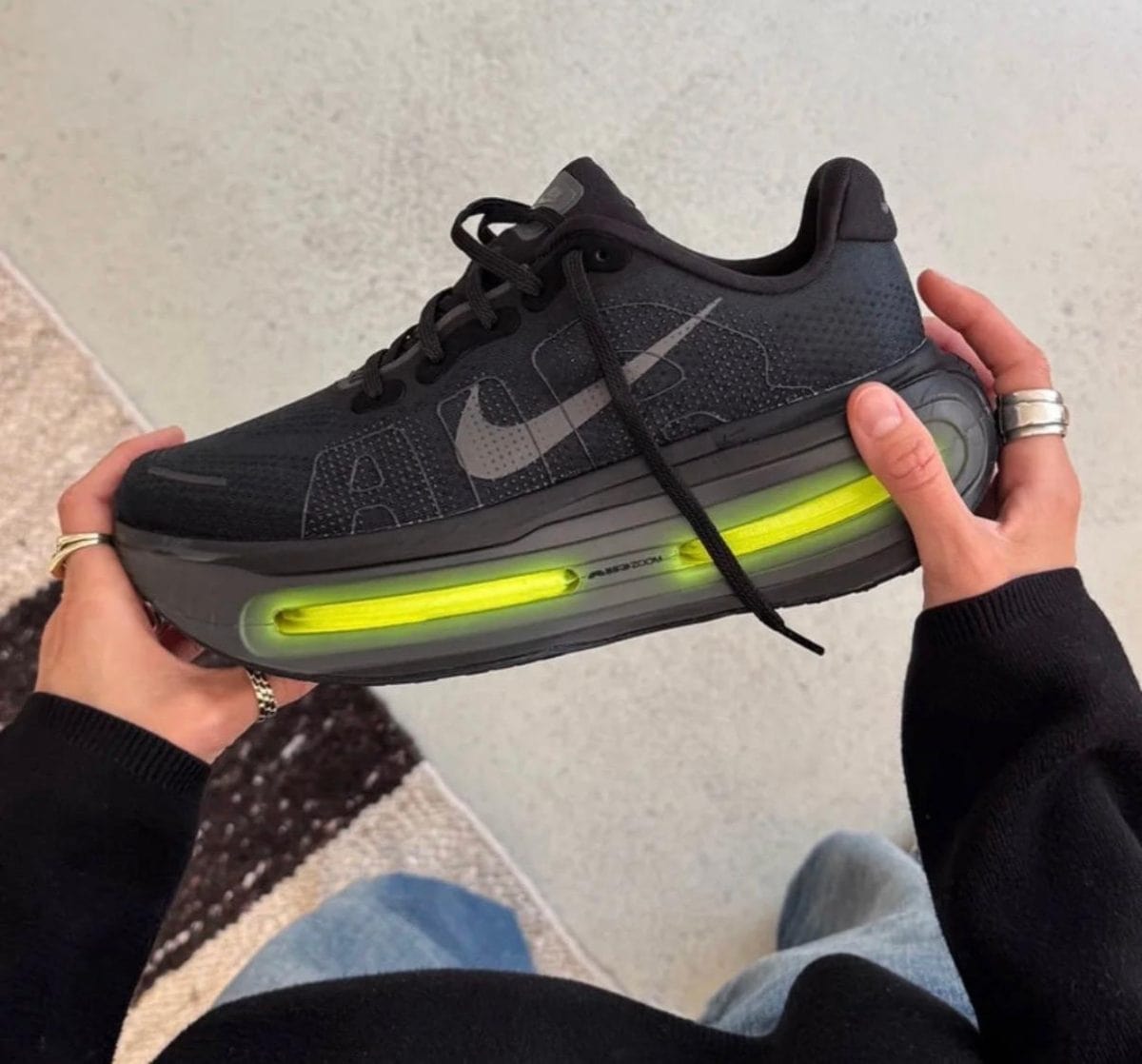Black Nike running shoe with a bright neon-green air cushion midsole, held by a person in a black sleeve.