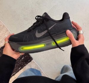 7fe4fb14-8075-4ce4-a0ba-775e421ffa0e | UAE SPORT STORE Black Nike running shoe with a bright neon-green air cushion midsole, held by a person in a black sleeve.