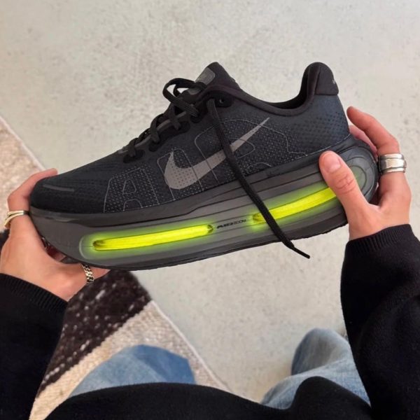 Black Nike running shoe with a bright neon-green air cushion midsole, held by a person in a black sleeve.