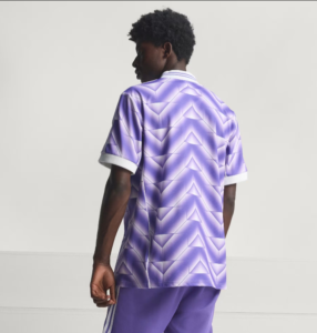 Back view of a person wearing a purple geometric-patterned polo jersey with white cuffs and matching shorts, standing against a light background.
