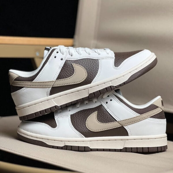 Pair of white and brown Nike sneakers with beige swoosh, stacked one on top of the other on a soft surface.