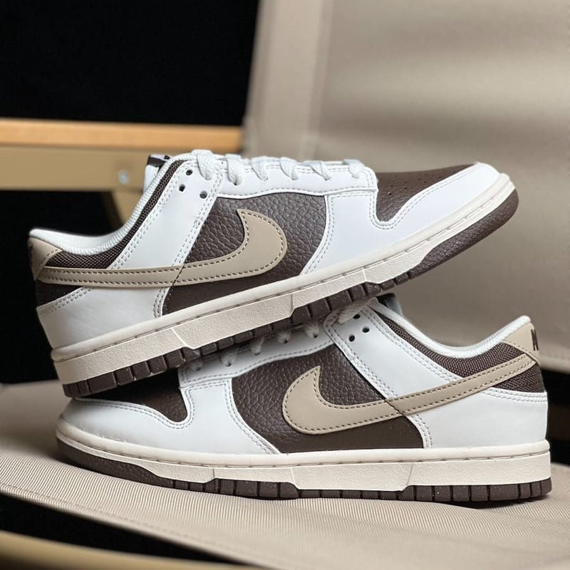 800x Pair of white and brown Nike sneakers with beige swoosh, stacked one on top of the other on a soft surface.