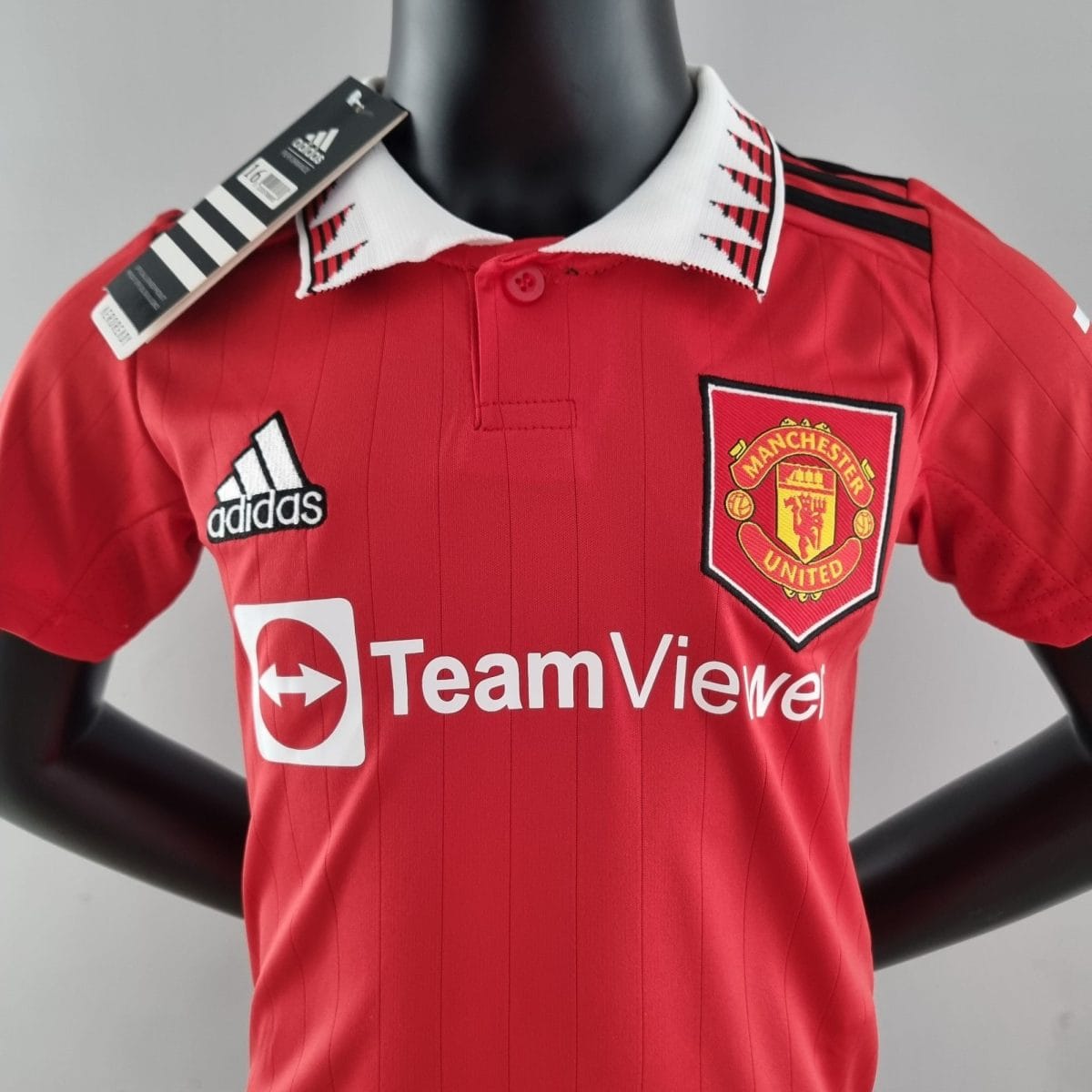 Manchester United red football jersey on a black mannequin with tag attached, showing team crest on the chest.