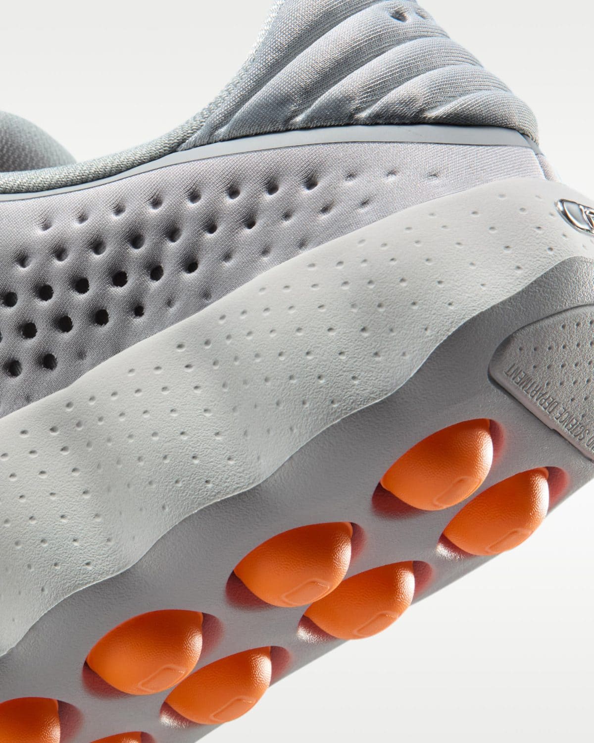 Close-up of a grey athletic shoe sole with orange traction pods and perforated white midsole detail.