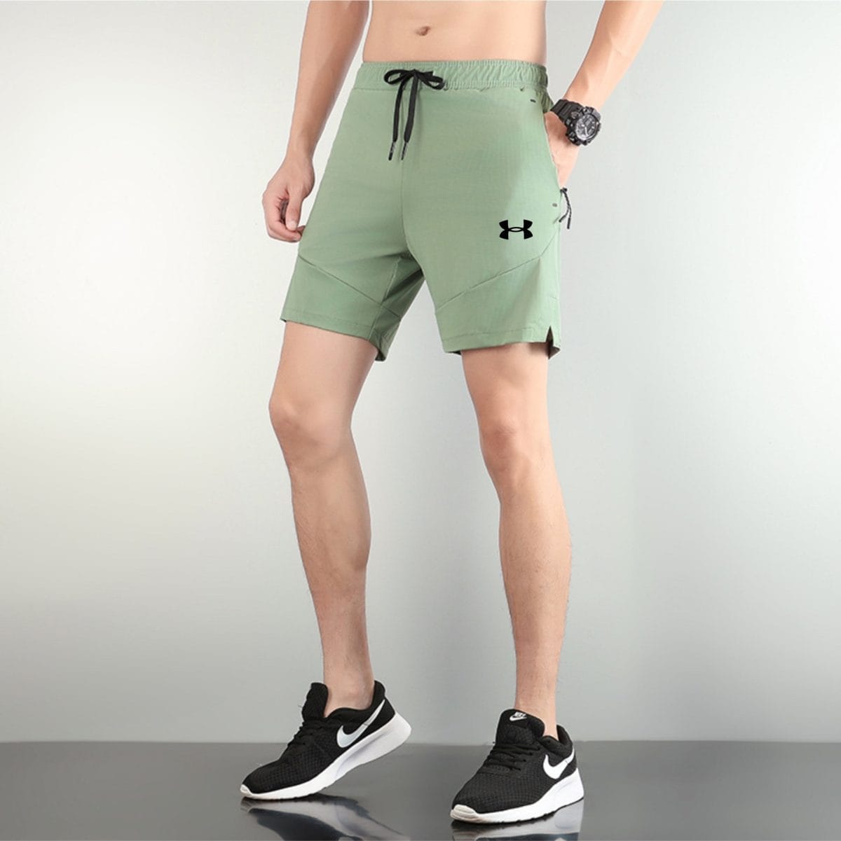 Person wearing sage-green athletic shorts and black Nike sneakers, standing on a gym floor.