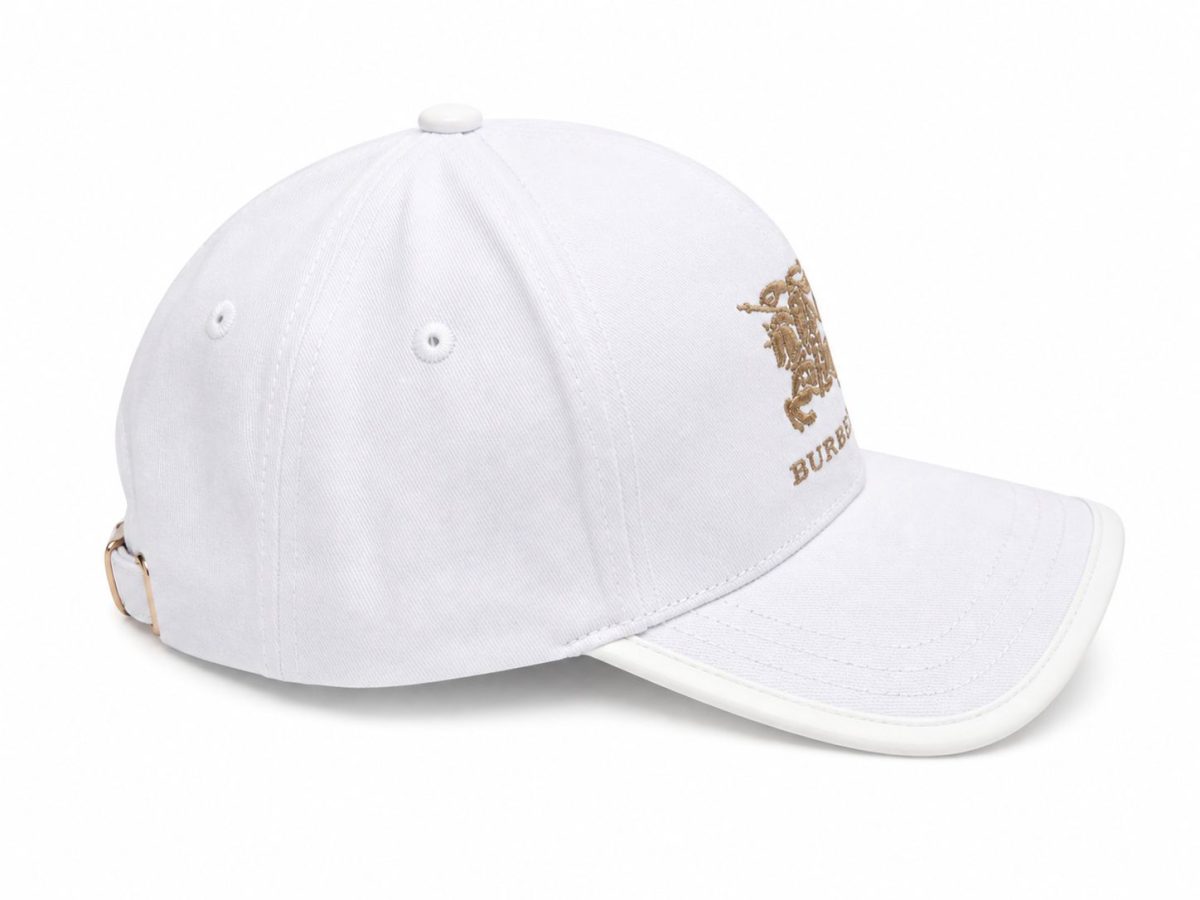 White baseball cap with gold Burberry emblem on the front and an adjustable strap on the back left side.