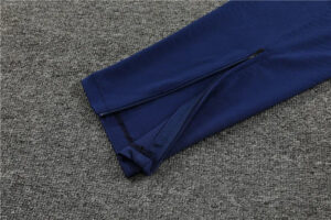 Blue athletic pants with an ankle zipper laid on a gray carpet.