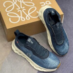 Pair of dark denim athletic sneakers with a chunky white sole, placed next to a brown shoebox with white branding.