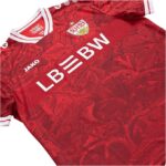 Red soccer jersey with crest on chest, white collar trim, and sponsor text across front (JAKO logo visible).