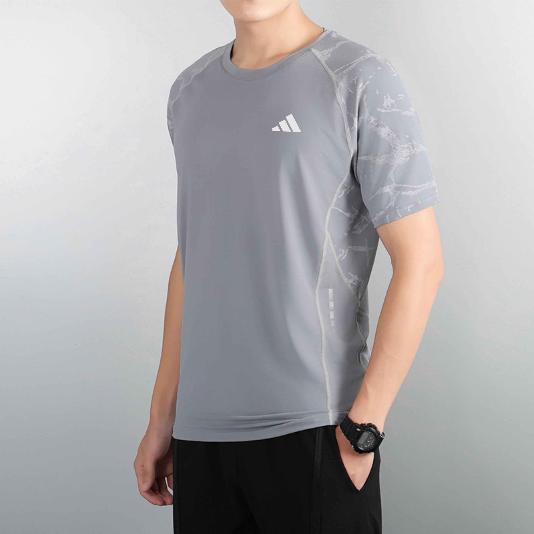 82531c33 | UAE SPORT STORE Person in a gray athletic shirt with a small white logo on the chest, standing against a pale wall, wearing a black watch on the left wrist.