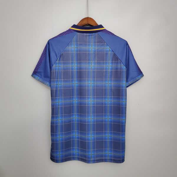 Blue plaid shirt or jacket on wooden hanger, back view, hanging against a light wall with purple sleeves and yellow trim on the collar.