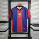 Barcelona football jersey with vertical red and blue stripes hanging on a wooden hanger in a metal display rack; features club crest and Nike swoosh