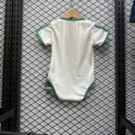 White baby onesie with green trim hanging on a wooden hanger against a metal grid wall, tag visible at the bottom left.