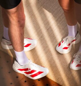 Close-up of white athletic sneakers with red stripes and white socks on a light floor.