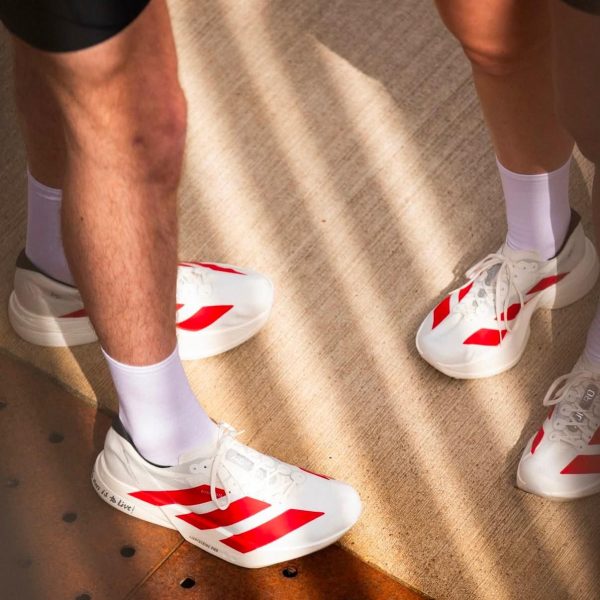 Close-up of white athletic sneakers with red stripes and white socks on a light floor.