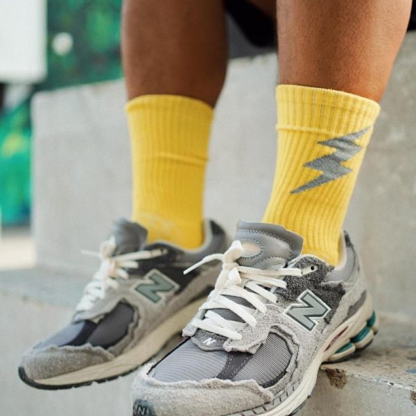 Close-up of a person wearing yellow socks with a gray lightning bolt design and gray sneakers standing on concrete steps.