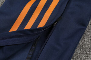 Close-up of navy fabric with two orange stripes and a black zipper along a pocket seam, likely on a jacket or bag edge.