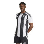 Male model wearing a black-and-white Juventus football jersey, standing with hands behind back against a white background.