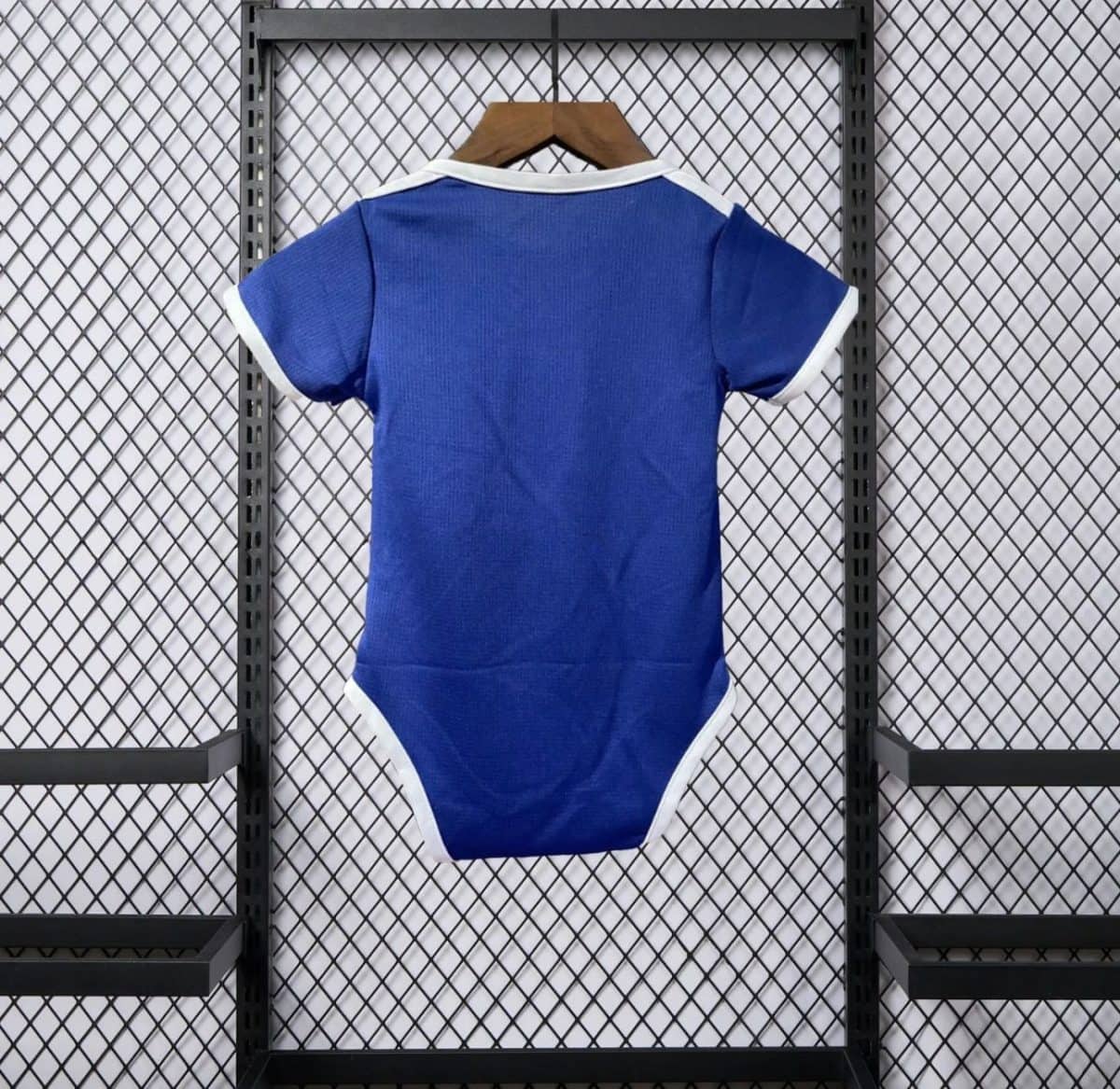 Blue infant onesie with white trim hanging on a wooden hanger against a metal mesh display backdrop