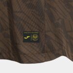 Close-up of brown textured fabric with a small black patch showing a gold Joma logo and Brentford FC crest.