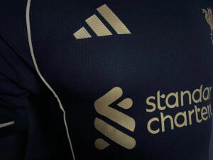 Close-up of a dark sports jersey showing the Adidas logo and Standard Chartered branding in light print.