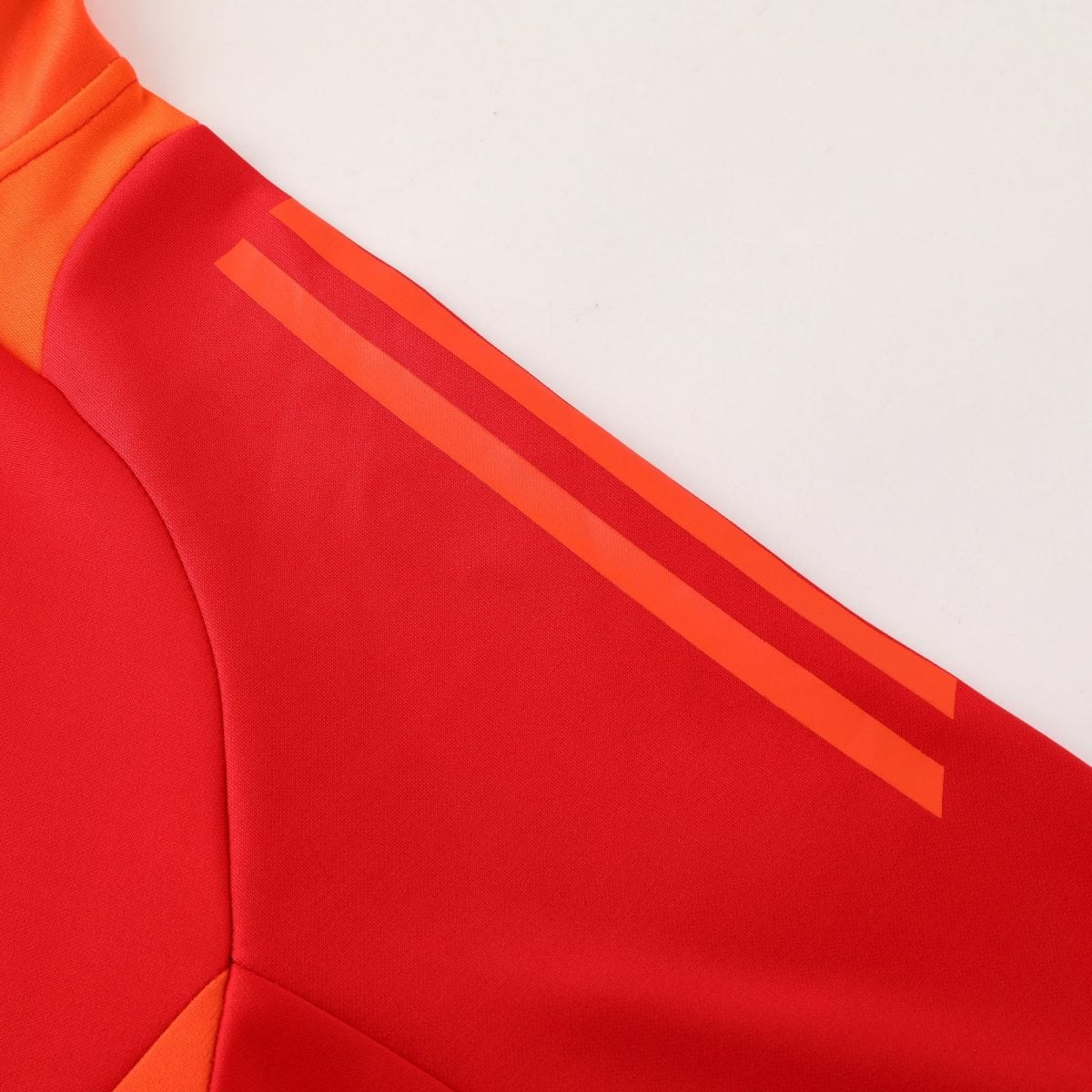 Close-up of red fabric with orange diagonal stripes on a garment, suggesting sporty outerwear detail.