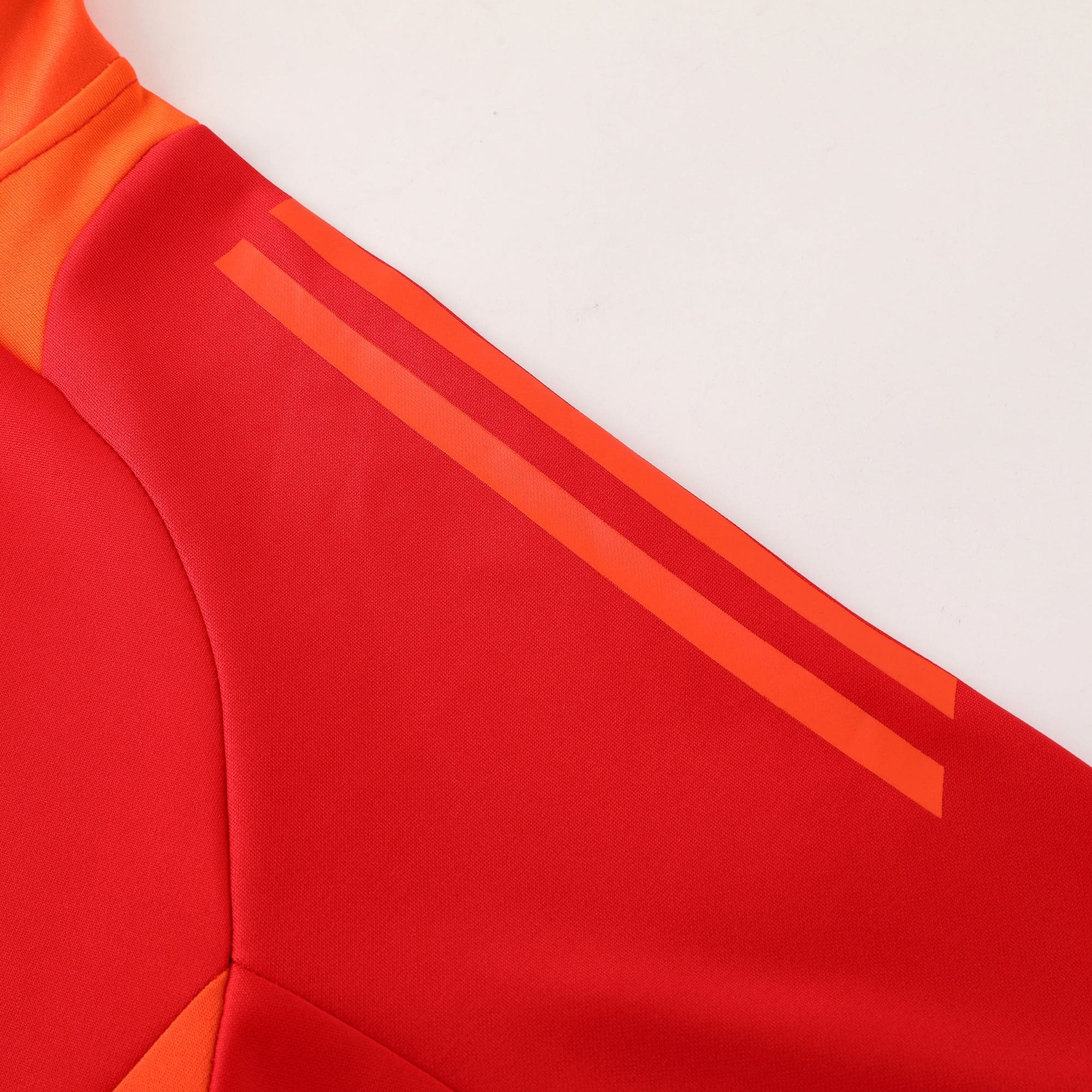 85806358 | UAE SPORT STORE Close-up of red fabric with orange diagonal stripes on a garment, suggesting sporty outerwear detail.